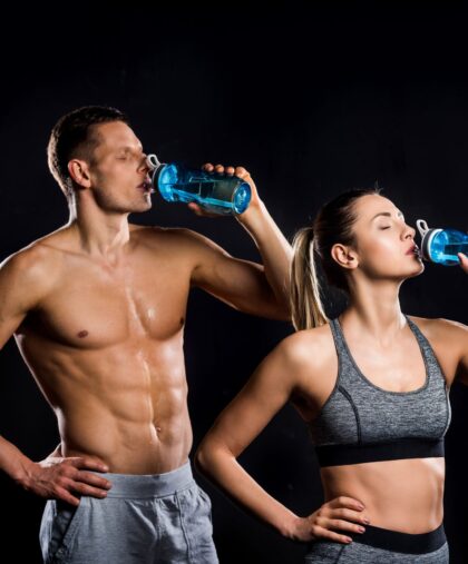 athletic young couple in sportswear drinking from bottles isolated on black